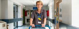 A female hospital worker with a healthcare ID badge pushing a trolly down a walkway.